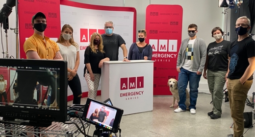 A group of people, wearing medical masks, stand in a television studio.